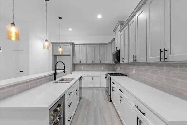 kitchen with wine cooler, sink, decorative light fixtures, stainless steel appliances, and light wood-type flooring