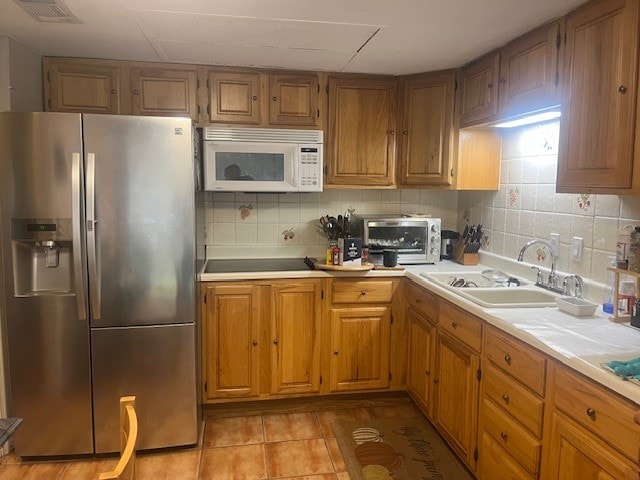 kitchen with tasteful backsplash, sink, stainless steel refrigerator with ice dispenser, light tile patterned floors, and black electric cooktop