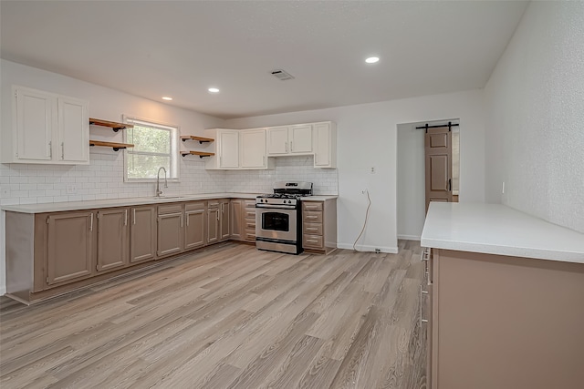 kitchen with sink, light wood-type flooring, a barn door, gas stove, and decorative backsplash