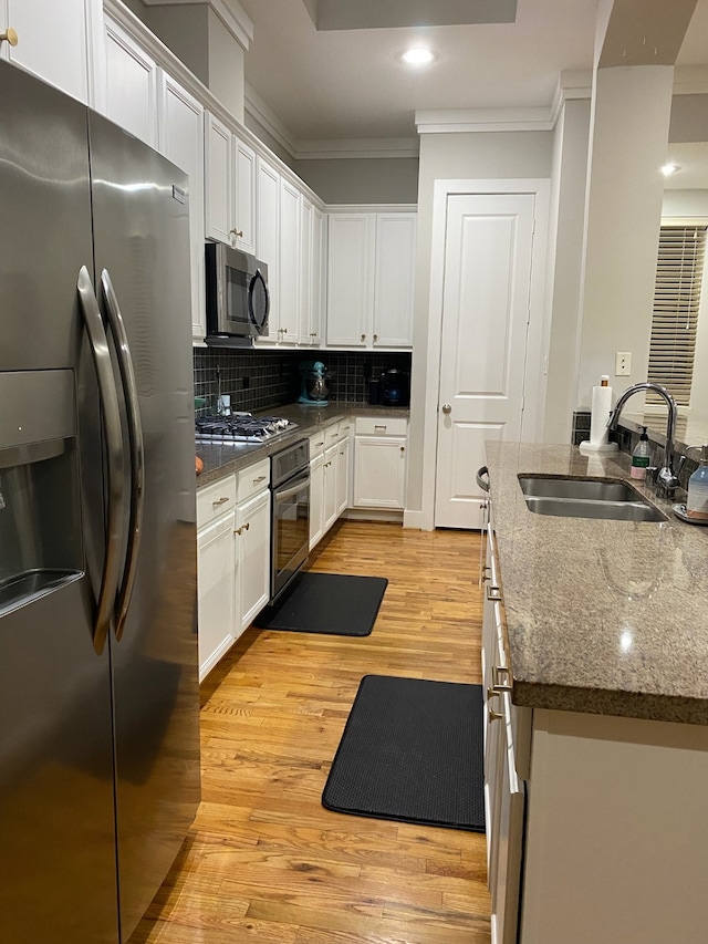 kitchen with sink, stainless steel appliances, tasteful backsplash, white cabinets, and light wood-type flooring