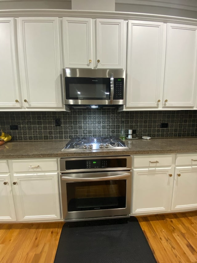 kitchen featuring backsplash, white cabinetry, stainless steel appliances, and light wood-type flooring