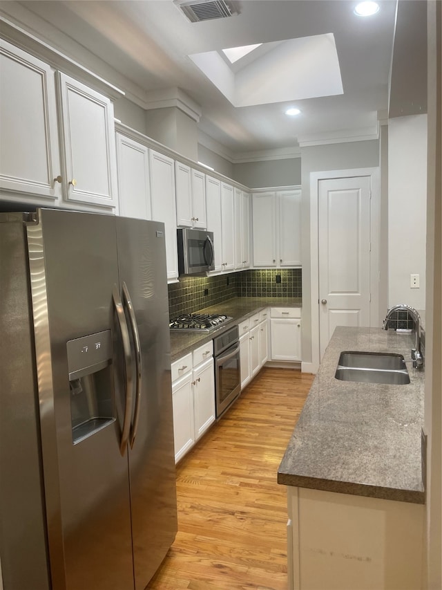 kitchen with a skylight, sink, stainless steel appliances, decorative backsplash, and white cabinets