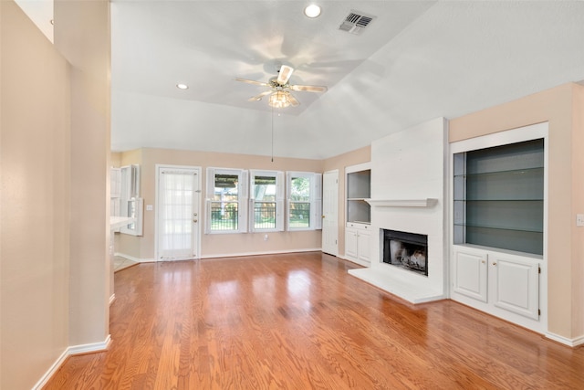 unfurnished living room featuring light wood-type flooring, lofted ceiling, a large fireplace, and ceiling fan