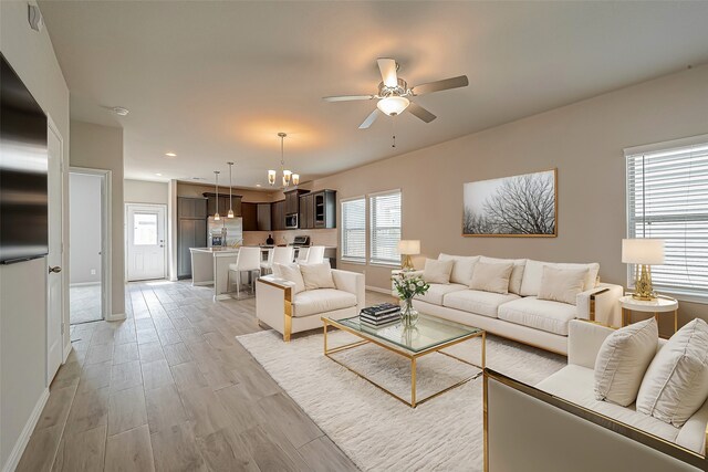 living room featuring ceiling fan with notable chandelier and light hardwood / wood-style flooring