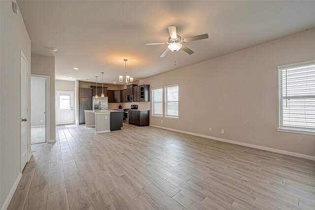 interior space with a kitchen island, light wood-type flooring, appliances with stainless steel finishes, dark brown cabinets, and decorative light fixtures