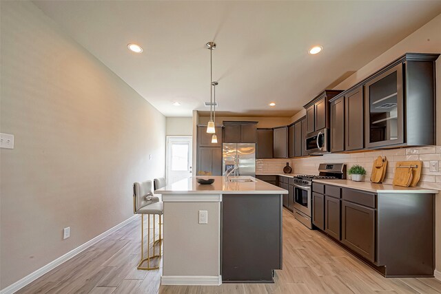 kitchen featuring sink, decorative light fixtures, a center island with sink, appliances with stainless steel finishes, and light wood-type flooring