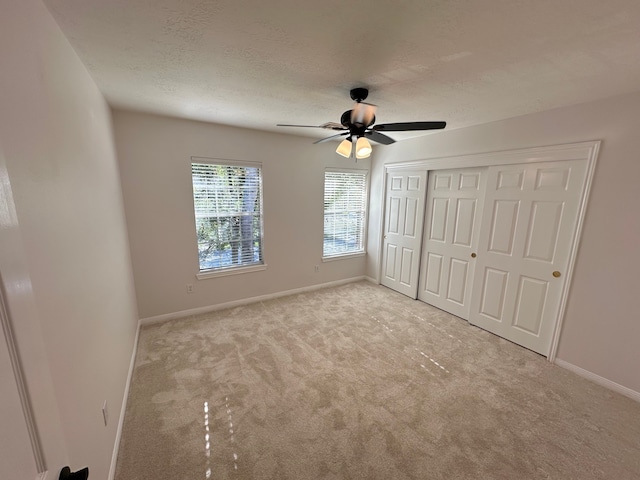 unfurnished bedroom featuring ceiling fan, light colored carpet, a textured ceiling, and a closet