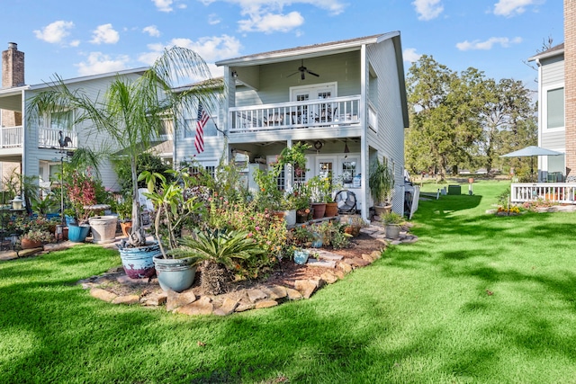 rear view of property with ceiling fan, a balcony, and a yard