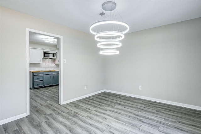 unfurnished dining area featuring an inviting chandelier and hardwood / wood-style flooring