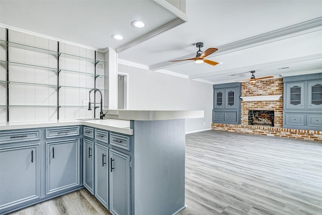 kitchen featuring crown molding, ceiling fan, a brick fireplace, kitchen peninsula, and light wood-type flooring