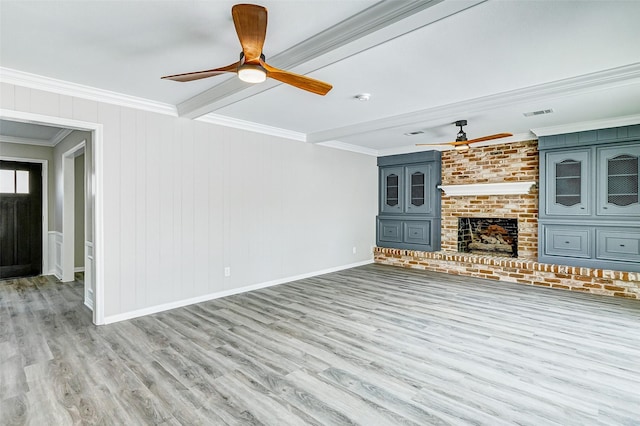 unfurnished living room featuring ornamental molding, beamed ceiling, ceiling fan, a fireplace, and light hardwood / wood-style floors