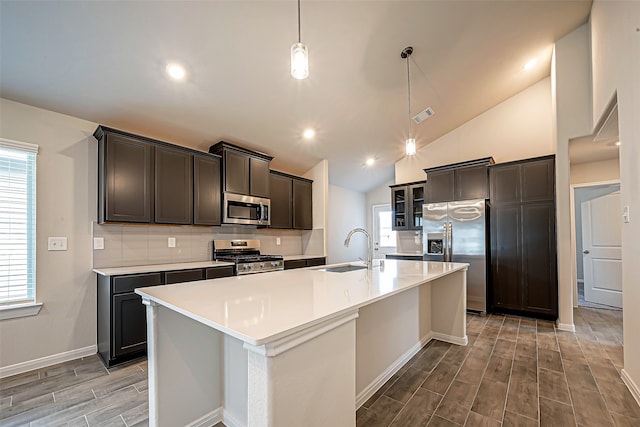 kitchen with stainless steel appliances, hanging light fixtures, a kitchen island with sink, and sink