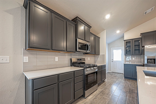 kitchen with decorative backsplash, light hardwood / wood-style flooring, stainless steel appliances, lofted ceiling, and a textured ceiling