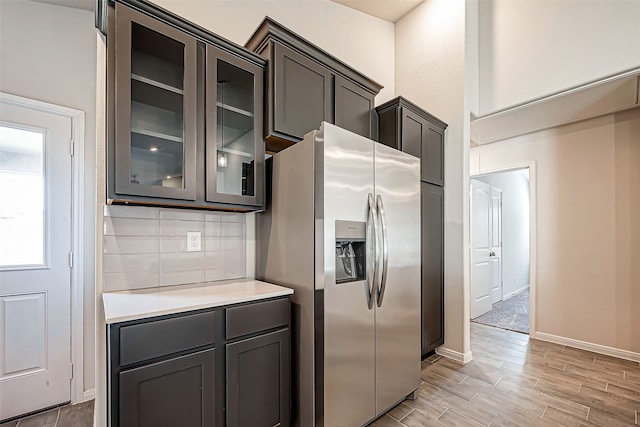 kitchen with dark brown cabinetry, stainless steel refrigerator with ice dispenser, light hardwood / wood-style floors, and decorative backsplash