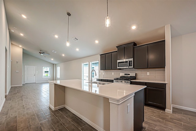 kitchen featuring decorative light fixtures, a center island with sink, sink, stainless steel appliances, and lofted ceiling