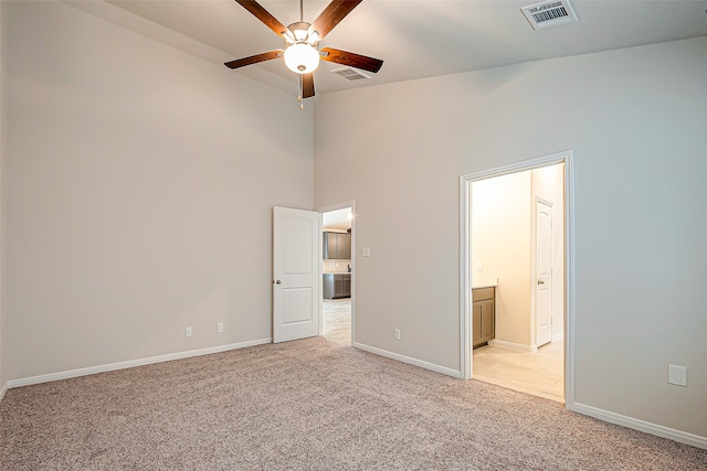 unfurnished bedroom featuring ceiling fan, ensuite bath, light carpet, and a towering ceiling