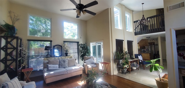 living room with hardwood / wood-style flooring, ceiling fan with notable chandelier, and a high ceiling