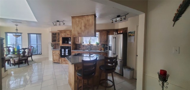 kitchen featuring stainless steel fridge with ice dispenser, a kitchen bar, rail lighting, oven, and light tile patterned floors