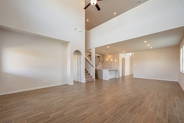 unfurnished living room with wood-type flooring, a high ceiling, and ceiling fan