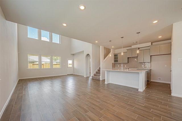 kitchen featuring a high ceiling, gray cabinetry, dark hardwood / wood-style flooring, decorative light fixtures, and an island with sink