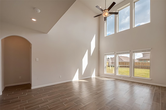 unfurnished living room with ceiling fan, a towering ceiling, and dark wood-type flooring