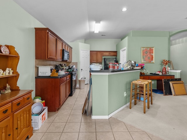 kitchen featuring light tile patterned flooring, tasteful backsplash, lofted ceiling, a kitchen breakfast bar, and black appliances