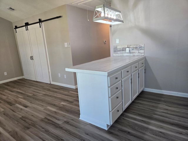 kitchen with dark wood-type flooring, baseboards, tile counters, and visible vents