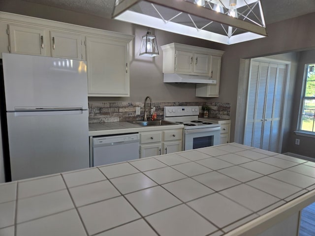 kitchen featuring white appliances, white cabinetry, under cabinet range hood, tile countertops, and a sink