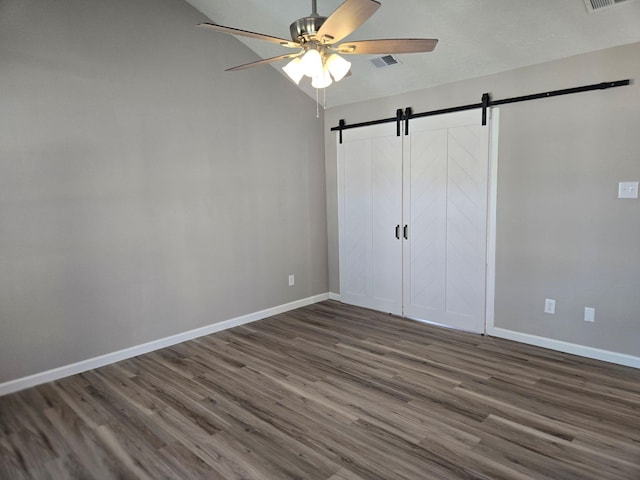 unfurnished bedroom featuring dark wood-type flooring, visible vents, baseboards, and a barn door