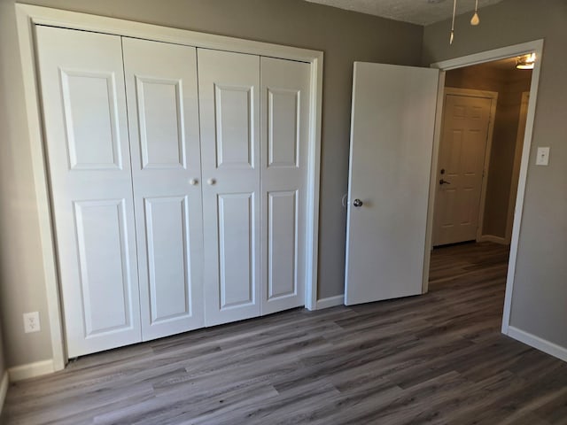 unfurnished bedroom featuring dark wood-style floors, a closet, and baseboards
