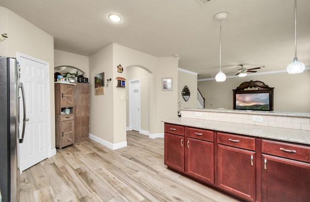 kitchen featuring light stone counters, hanging light fixtures, light hardwood / wood-style flooring, backsplash, and stainless steel refrigerator