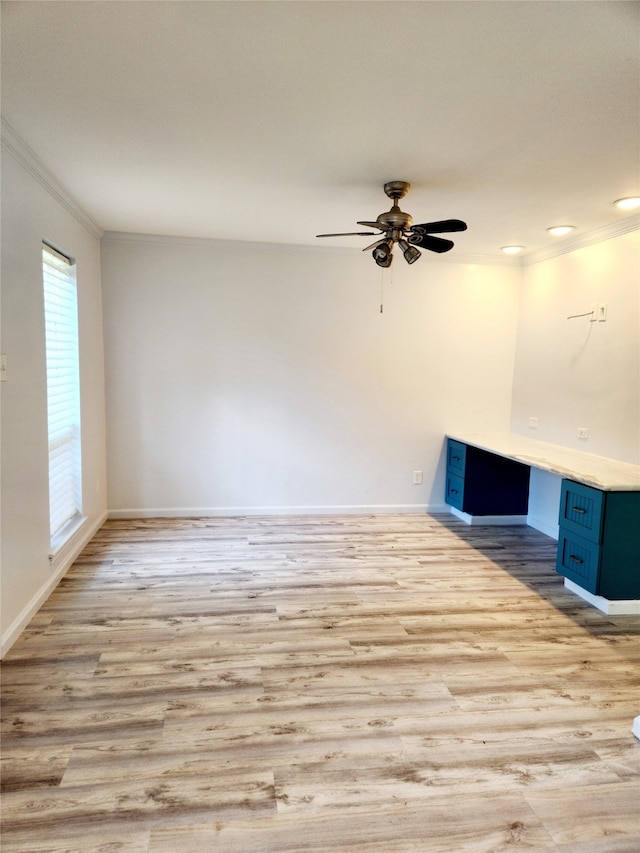 empty room with light hardwood / wood-style flooring, built in desk, ceiling fan, and crown molding