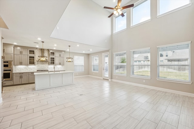 unfurnished living room featuring a towering ceiling, ceiling fan, and sink