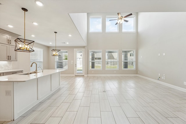 kitchen with pendant lighting, light hardwood / wood-style floors, sink, ceiling fan with notable chandelier, and a high ceiling