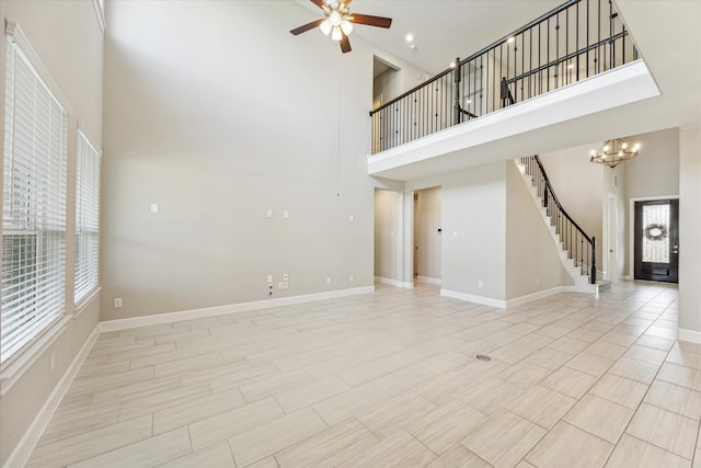 unfurnished living room with ceiling fan with notable chandelier, a towering ceiling, and plenty of natural light