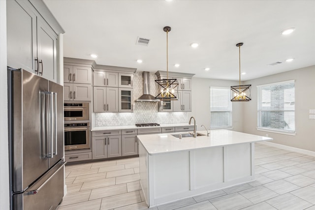 kitchen featuring an island with sink, sink, decorative light fixtures, wall chimney range hood, and stainless steel appliances