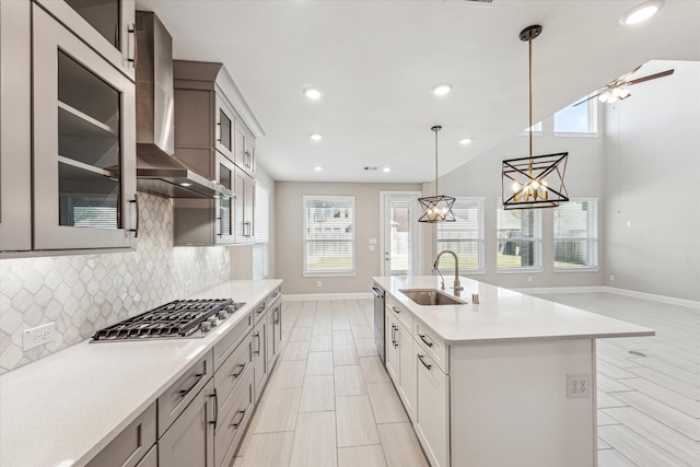 kitchen featuring sink, hanging light fixtures, wall chimney exhaust hood, a center island with sink, and appliances with stainless steel finishes