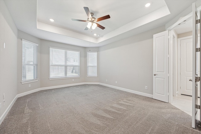 empty room featuring light colored carpet, ceiling fan, and a raised ceiling