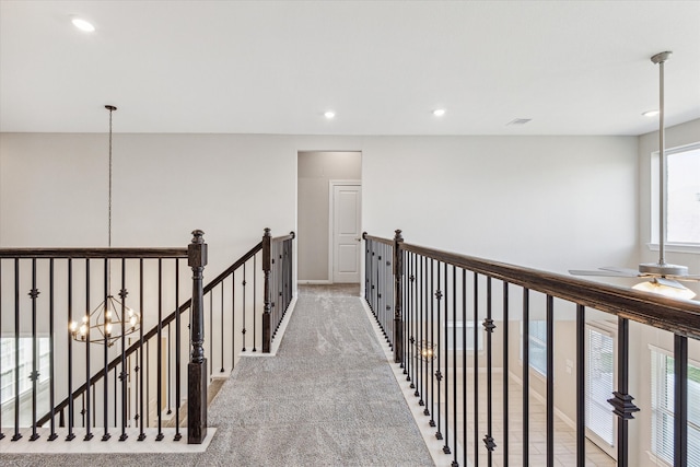 hall featuring light colored carpet, a notable chandelier, and a healthy amount of sunlight