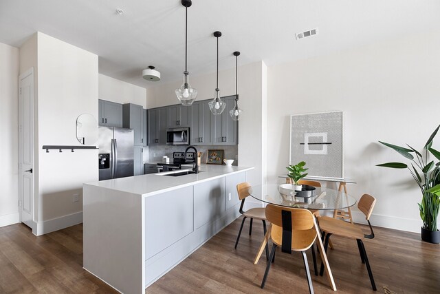 kitchen with appliances with stainless steel finishes, gray cabinetry, dark wood-type flooring, kitchen peninsula, and pendant lighting