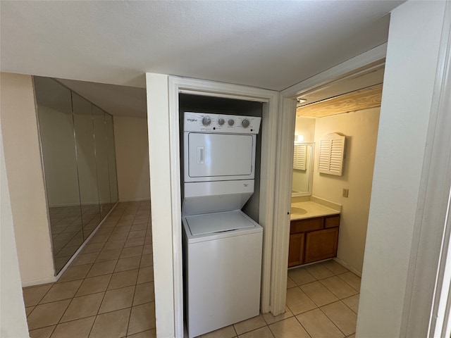 laundry area featuring light tile patterned flooring, stacked washer and clothes dryer, and a textured ceiling