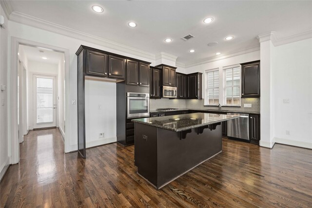 kitchen with dark stone countertops, sink, stainless steel appliances, dark hardwood / wood-style floors, and a center island