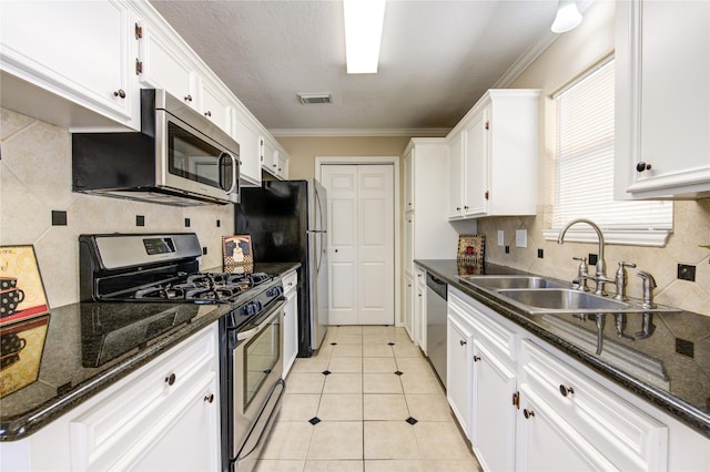 kitchen with appliances with stainless steel finishes, white cabinetry, sink, light tile patterned floors, and crown molding