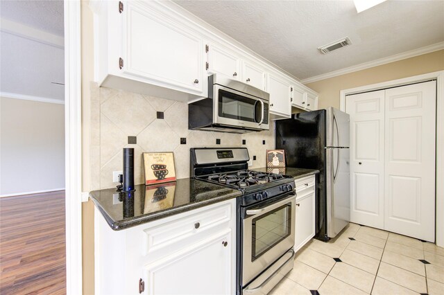 kitchen featuring light tile patterned floors, white cabinetry, appliances with stainless steel finishes, dark stone countertops, and crown molding