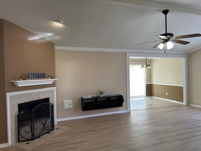 unfurnished living room with crown molding, wood-type flooring, a tiled fireplace, and ceiling fan