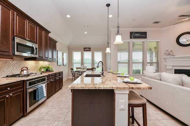 kitchen with appliances with stainless steel finishes, pendant lighting, lofted ceiling, a center island with sink, and sink