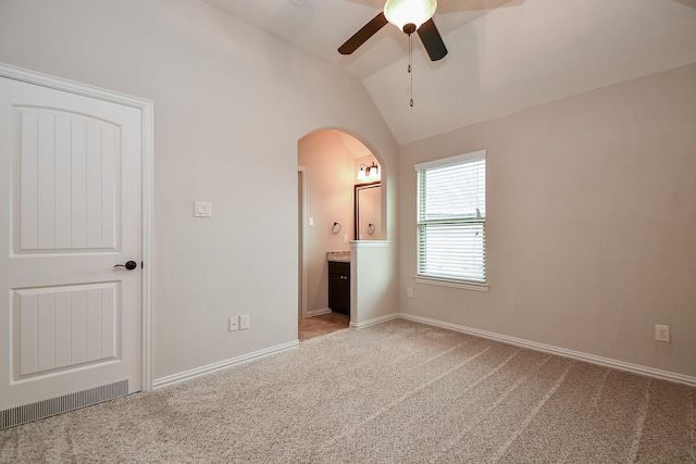 unfurnished bedroom featuring ceiling fan, lofted ceiling, light carpet, and ensuite bathroom