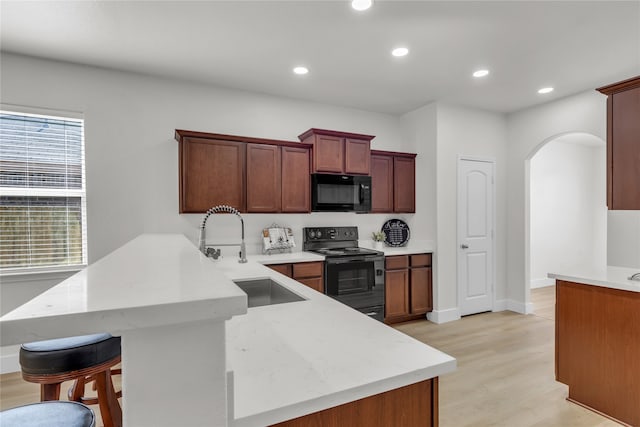 kitchen with a breakfast bar, kitchen peninsula, black appliances, light hardwood / wood-style flooring, and sink