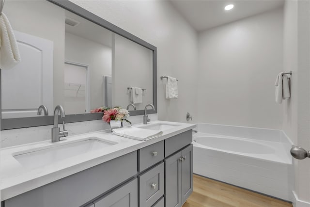 bathroom featuring a relaxing tiled tub, hardwood / wood-style flooring, and vanity