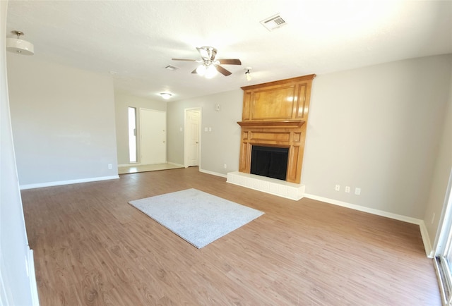 unfurnished living room with ceiling fan, hardwood / wood-style flooring, and a large fireplace